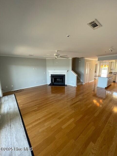 unfurnished living room with light wood-type flooring, a fireplace with flush hearth, visible vents, and ceiling fan