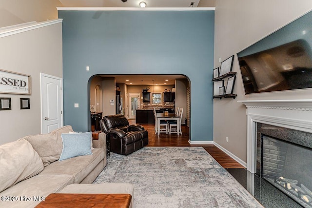 living area featuring arched walkways, a fireplace with flush hearth, baseboards, and dark wood-style flooring