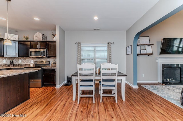 dining space featuring a fireplace, light wood-style floors, arched walkways, and baseboards