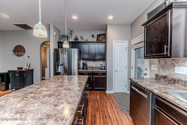 kitchen with arched walkways, dark brown cabinets, appliances with stainless steel finishes, and wood finished floors