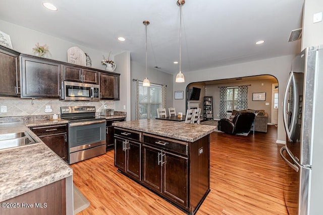 kitchen with tasteful backsplash, a kitchen island, dark brown cabinetry, appliances with stainless steel finishes, and arched walkways