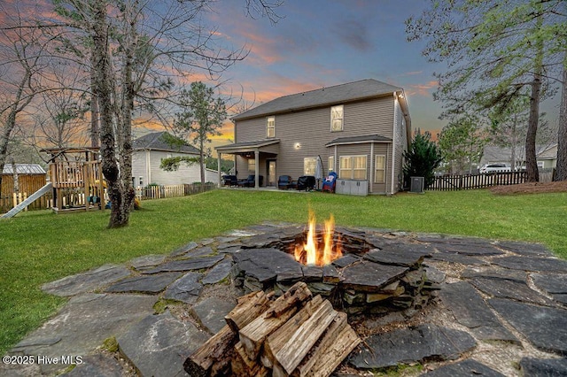 rear view of property featuring a lawn, a fire pit, a playground, and fence