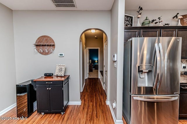 kitchen with visible vents, baseboards, wood finished floors, arched walkways, and stainless steel fridge