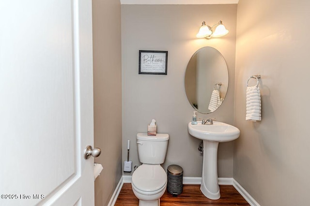 bathroom with toilet, wood finished floors, baseboards, and a sink