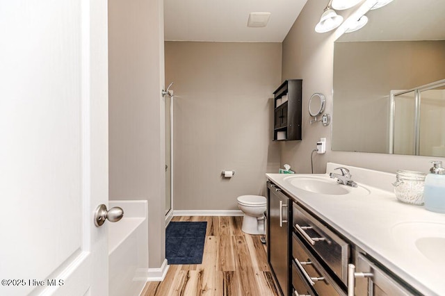 bathroom with toilet, a sink, wood finished floors, a shower stall, and double vanity