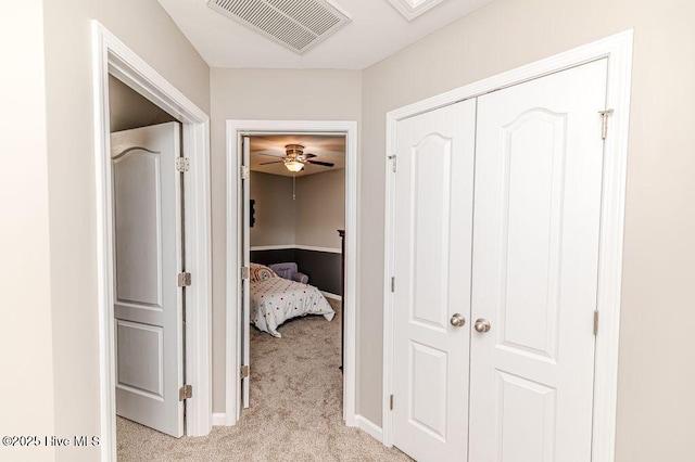 hallway featuring baseboards, visible vents, and light carpet