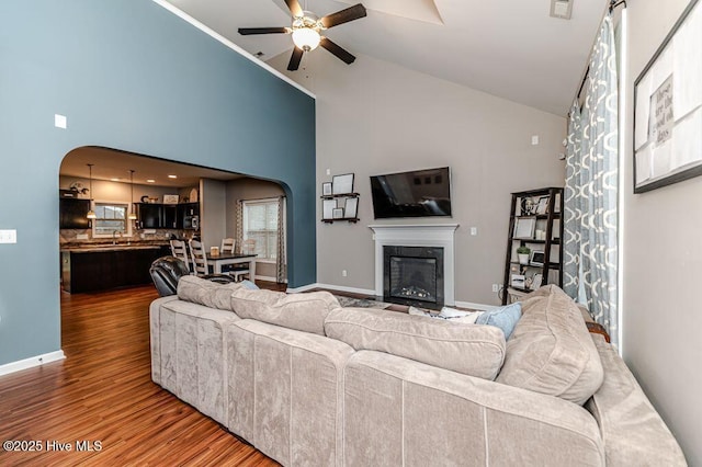 living area featuring arched walkways, a glass covered fireplace, a ceiling fan, and wood finished floors