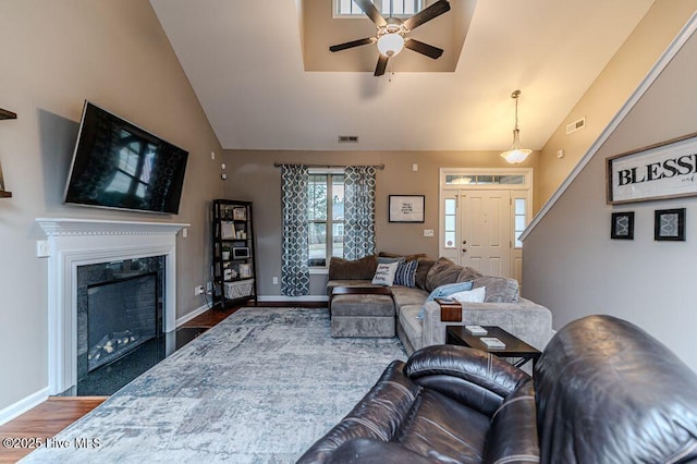 living room with visible vents, wood finished floors, baseboards, a fireplace, and lofted ceiling