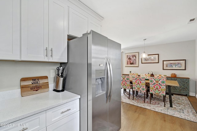 kitchen with visible vents, light stone counters, light wood-style floors, stainless steel refrigerator with ice dispenser, and white cabinetry