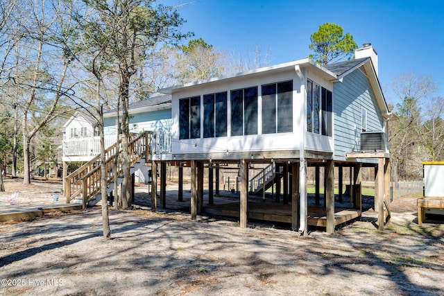 rear view of house with driveway, stairway, a sunroom, a carport, and a chimney