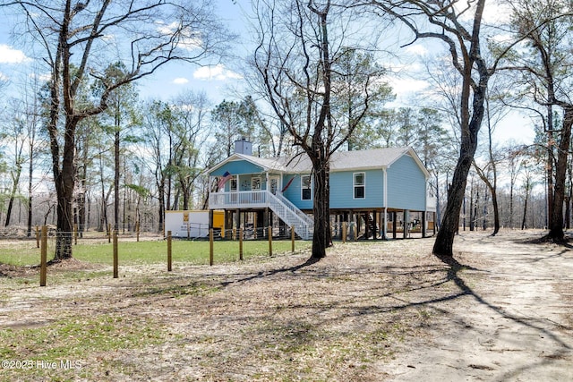 view of front of property with a front lawn, dirt driveway, a porch, stairs, and a chimney