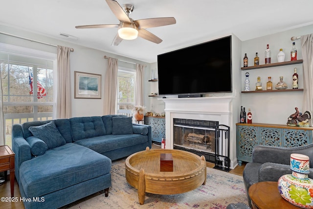 living room with visible vents, ceiling fan, a fireplace with flush hearth, and wood finished floors