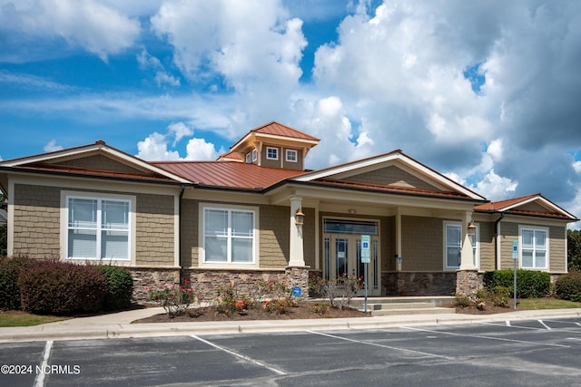 view of front facade featuring metal roof, stone siding, uncovered parking, and a standing seam roof