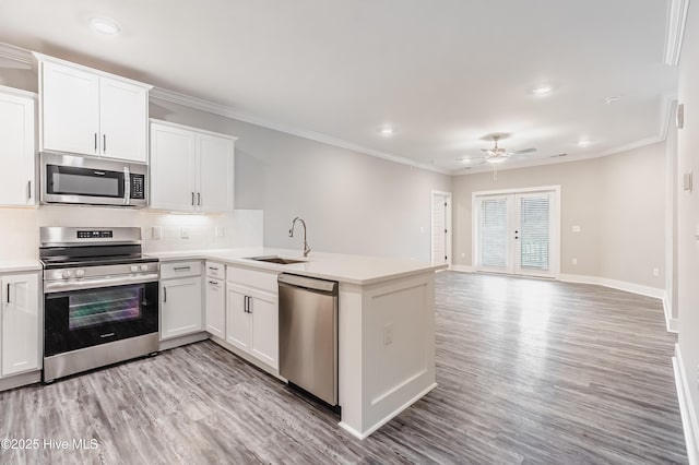 kitchen featuring a sink, tasteful backsplash, stainless steel appliances, a peninsula, and crown molding