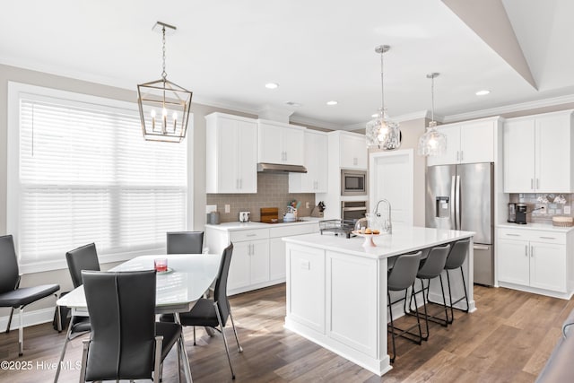 kitchen with a kitchen bar, under cabinet range hood, appliances with stainless steel finishes, white cabinets, and light countertops