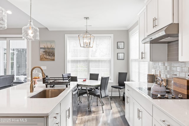 kitchen featuring a sink, light countertops, under cabinet range hood, tasteful backsplash, and a chandelier