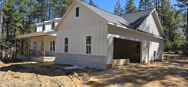 view of side of home featuring stone siding, covered porch, board and batten siding, and a shingled roof