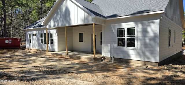 rear view of house featuring board and batten siding, covered porch, and a shingled roof