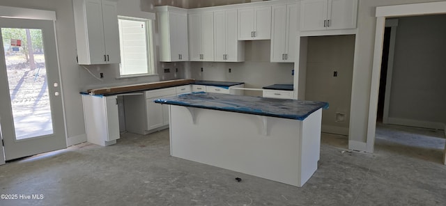 kitchen featuring a kitchen bar, dark countertops, a center island, and white cabinetry