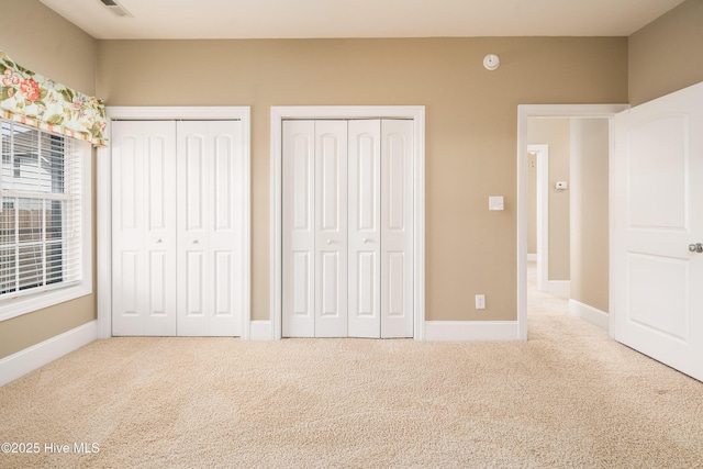 unfurnished bedroom featuring carpet flooring, baseboards, and two closets