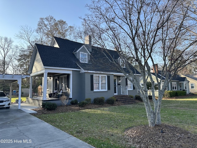 new england style home featuring a front yard, roof with shingles, driveway, covered porch, and a chimney