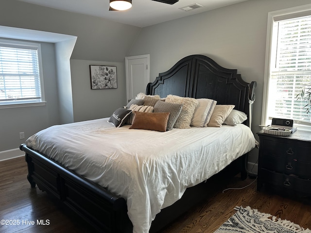 bedroom with visible vents, lofted ceiling, baseboards, and dark wood finished floors