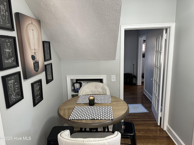 dining room featuring a textured ceiling, dark wood-type flooring, baseboards, and vaulted ceiling