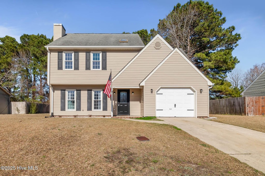 colonial house with a front yard, concrete driveway, a chimney, and fence