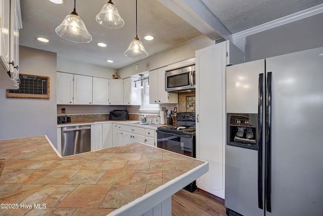 kitchen featuring pendant lighting, a textured ceiling, tile countertops, stainless steel appliances, and white cabinets