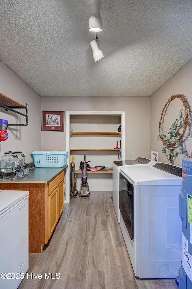 clothes washing area featuring cabinet space, water heater, light wood-style floors, a textured ceiling, and washing machine and dryer