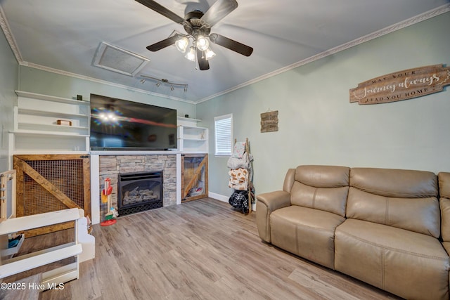 living room with a stone fireplace, crown molding, attic access, and wood finished floors