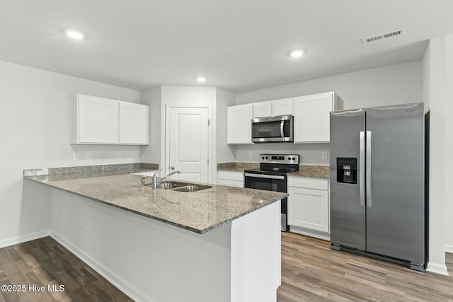 kitchen with visible vents, a peninsula, a sink, stainless steel appliances, and dark wood-type flooring