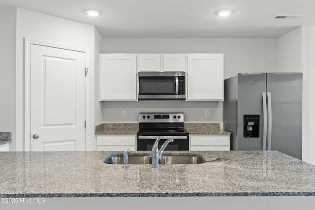 kitchen with stone counters, white cabinets, appliances with stainless steel finishes, and a sink