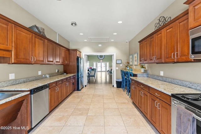 kitchen featuring light tile patterned floors, light stone countertops, brown cabinets, and stainless steel appliances
