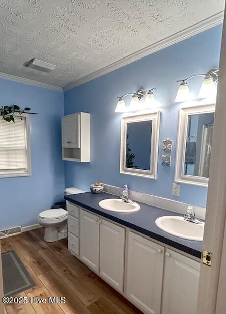 full bath featuring a sink, double vanity, wood finished floors, and crown molding