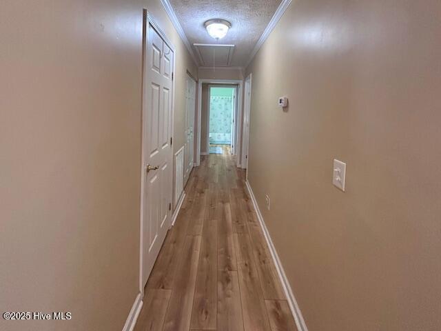 hallway with a textured ceiling, wood finished floors, crown molding, baseboards, and attic access