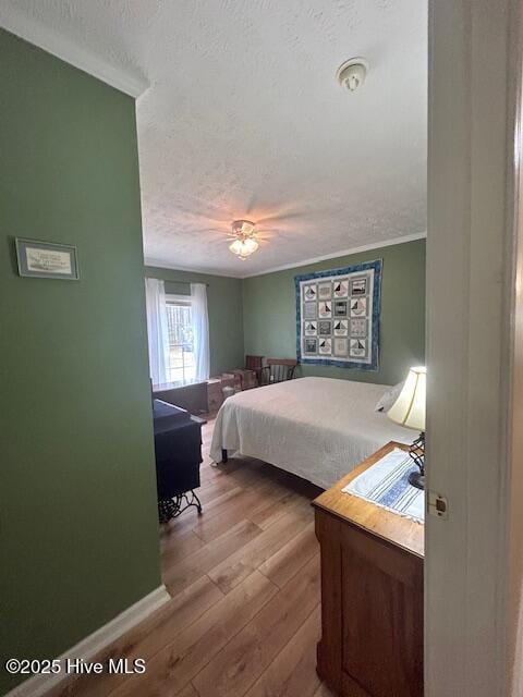 bedroom with crown molding, wood finished floors, baseboards, and a textured ceiling