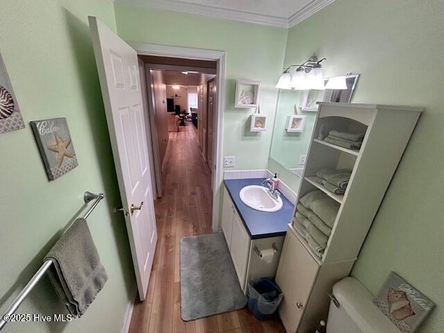 half bathroom featuring ornamental molding, vanity, toilet, and wood finished floors