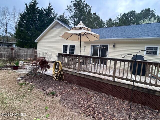 back of property with a wooden deck, roof with shingles, and fence