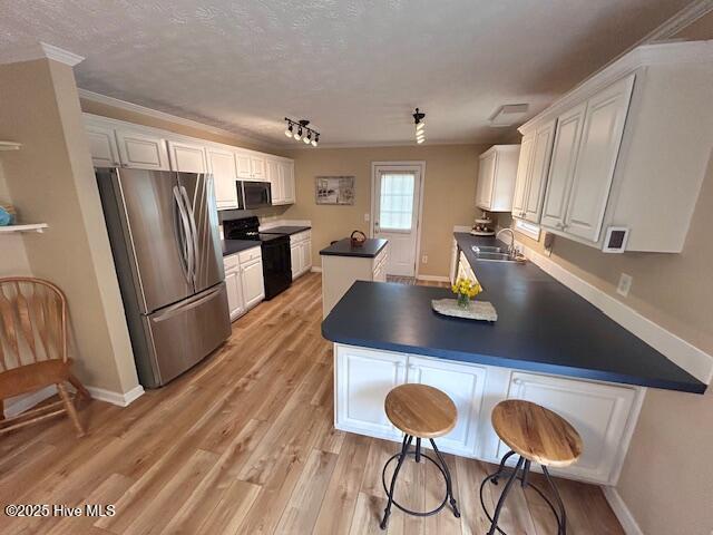 kitchen featuring black / electric stove, a peninsula, freestanding refrigerator, a sink, and white cabinets