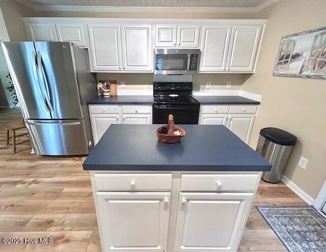 kitchen with dark countertops, light wood finished floors, ornamental molding, stainless steel appliances, and white cabinetry