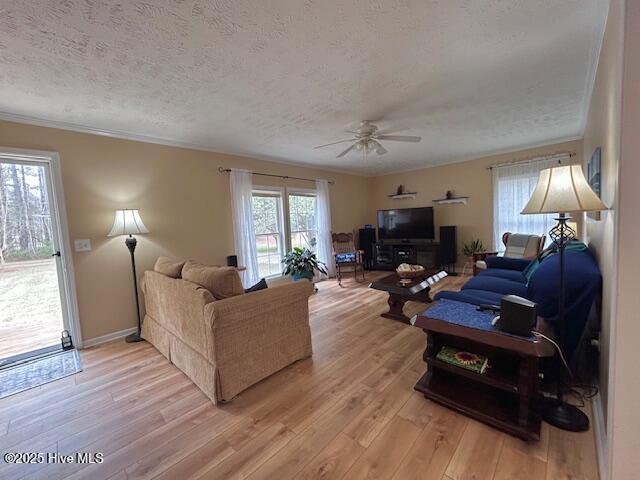 living area featuring light wood finished floors, baseboards, ornamental molding, a textured ceiling, and a ceiling fan