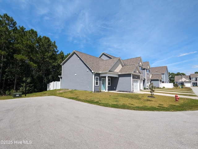 view of front of property featuring fence, driveway, roof with shingles, a front lawn, and a garage