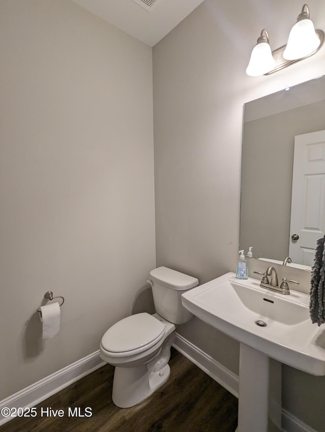 half bath with toilet, baseboards, and wood finished floors