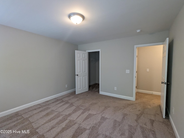 unfurnished bedroom featuring a walk in closet, baseboards, and carpet