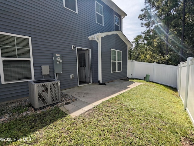 rear view of house with central air condition unit, a patio, a lawn, and a fenced backyard