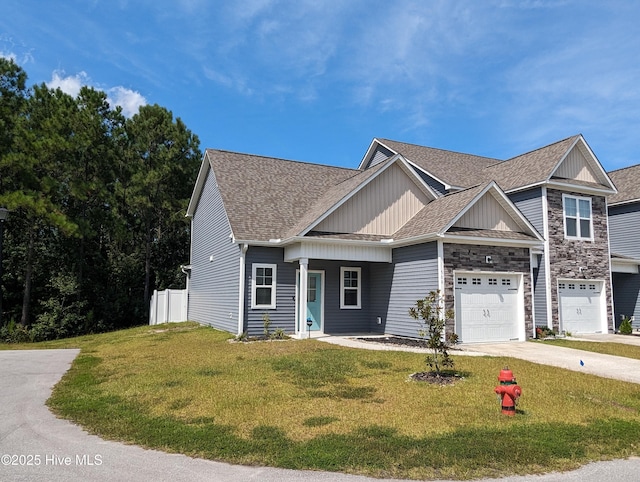 view of front of property featuring stone siding, roof with shingles, concrete driveway, and a front yard