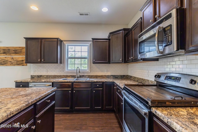 kitchen featuring backsplash, dark brown cabinetry, dark wood-style floors, stainless steel appliances, and a sink