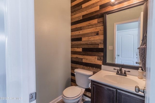 half bath featuring vanity, wooden walls, and toilet