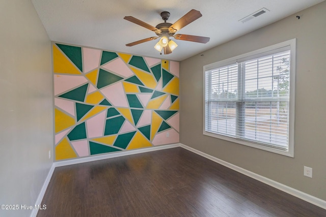 empty room with visible vents, an accent wall, baseboards, wood finished floors, and a ceiling fan